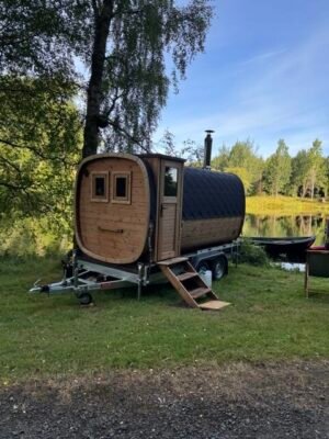 Widok z boku mobilnej sauny TimberIN Nordic Square na przyczepie z kominem nad jeziorem
