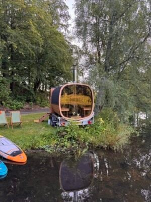 Widok z tyłu z panoramicznym przeszkleniem mobilnej sauny TimberIN Nordic Square na przyczepie nad jeziorem